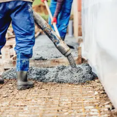 Pracownicy wylewają beton. Warto wiedzieć, ile waży kubik betonu, by zaplanować budowę.