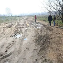 Ludzie spacerują po błotnistej drodze, gdzie minimalna odległość drogi wewnętrznej od granicy działki jest widoczna na tle mglistego krajobrazu.
