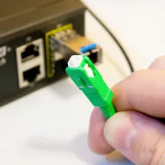 Zielona wtyczka światłowodu gotowa do podłączenia do switcha w bloku. Szybki internet w zasięgu ręki.