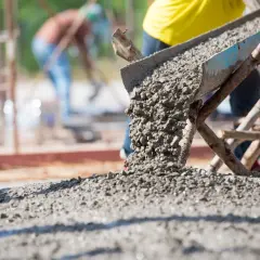 Beton wylewany z betoniarki na placu budowy. Obrazek ilustruje, jak obliczyć metry sześcienne betonu potrzebne do wylania fundamentów.