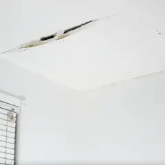 Widoczny pęknięcie na suficie w bloku, odsłaniające fragmenty konstrukcji. Obok okno z białymi żaluzjami.