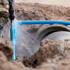 Wyciek wody z niebieskiej rury, widoczny w wykopie obok betonowych rur kanalizacyjnych, może wskazywać, jak wykryć nielegalne przyłącze wody.