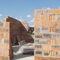 Budowa domu z pustaków ceramicznych. Widać ściany wznoszone z cegieł, które mają różne wymiary, tworząc konstrukcję.