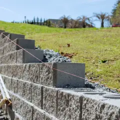 Budowa muru oporowego z bloczków betonowych. Najtaniej można go wykonać samodzielnie, używając prostych narzędzi i materiałów.