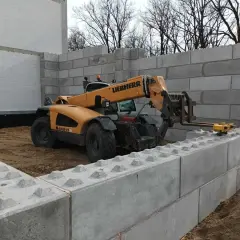 Żuraw budowlany stawia betonowe bloki, tworząc mur oporowy. Potrzebne jest pozwolenie na budowę.