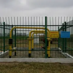 Ogrodzony obiekt gazowy z żółtymi rurami. Widać znaki ostrzegawcze. Obraz pokazuje odległość budynku od gazociągu wysokiego ciśnienia.