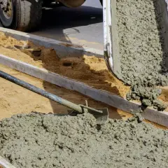 Betoniarka wylewa świeżą masę, z której się robi cement. Robotnik łopatą rozprowadza ją po wyznaczonym terenie.
