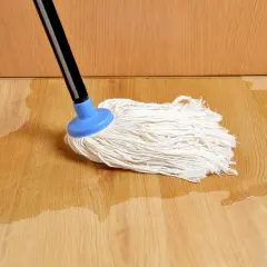Mop na mokrej podłodze. Woda rozlana na panelach sugeruje problem, jak naprawić odstający panel podłogowy.