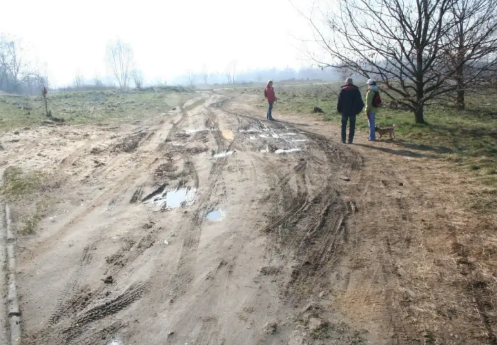 Ludzie spacerują po błotnistej drodze, gdzie minimalna odległość drogi wewnętrznej od granicy działki jest widoczna na tle mglistego krajobrazu.
