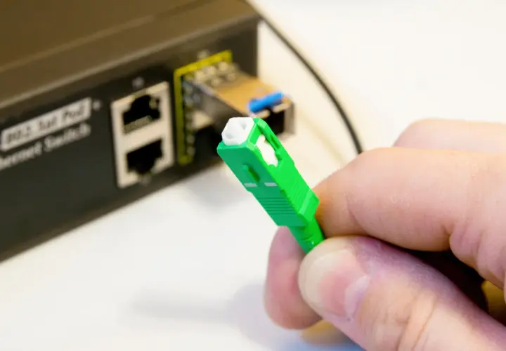 Zielona wtyczka światłowodu gotowa do podłączenia do switcha w bloku. Szybki internet w zasięgu ręki.