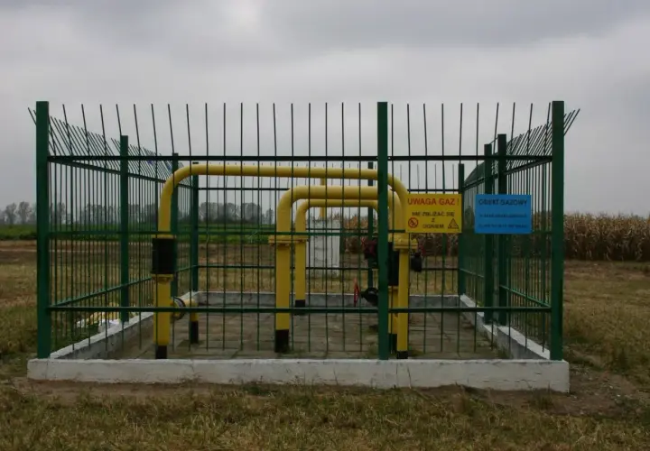 Ogrodzony obiekt gazowy z żółtymi rurami. Widać znaki ostrzegawcze. Obraz pokazuje odległość budynku od gazociągu wysokiego ciśnienia.