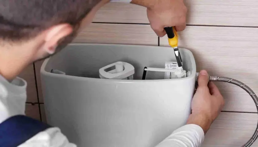 Instalator pokazuje, jak wyregulować spłuczkę, używając narzędzia do precyzyjnego ustawienia mechanizmu.