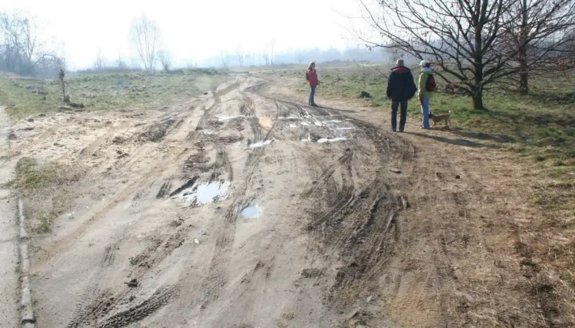 Ludzie spacerują po błotnistej drodze, gdzie minimalna odległość drogi wewnętrznej od granicy działki jest widoczna na tle mglistego krajobrazu.