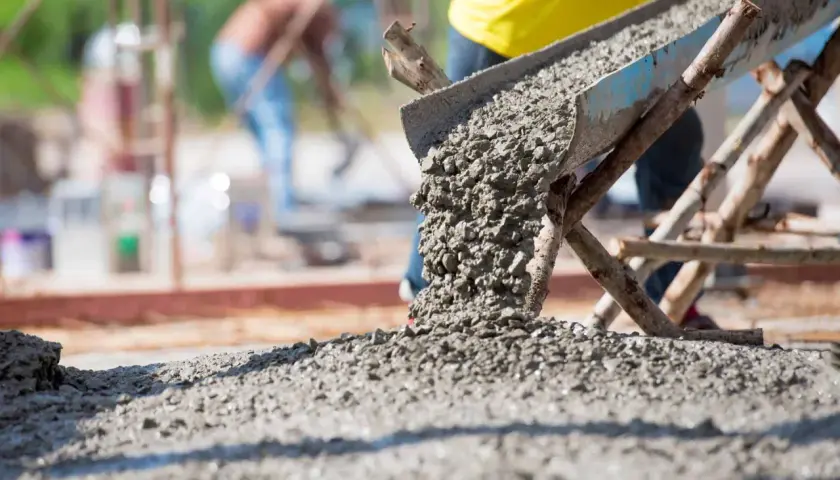 Beton wylewany z betoniarki na placu budowy. Obrazek ilustruje, jak obliczyć metry sześcienne betonu potrzebne do wylania fundamentów.
