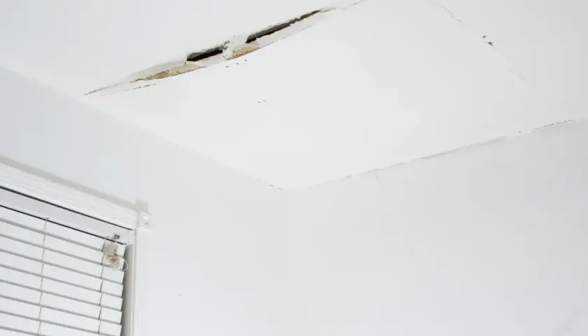 Widoczny pęknięcie na suficie w bloku, odsłaniające fragmenty konstrukcji. Obok okno z białymi żaluzjami.