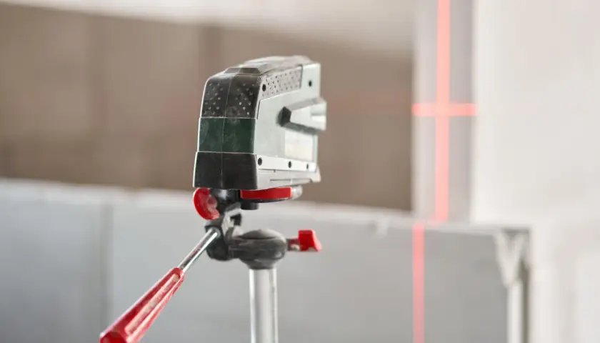 Poziomica laserowa na statywie z czerwonymi liniami wyznaczającymi idealny ranking poziomic laserowych.