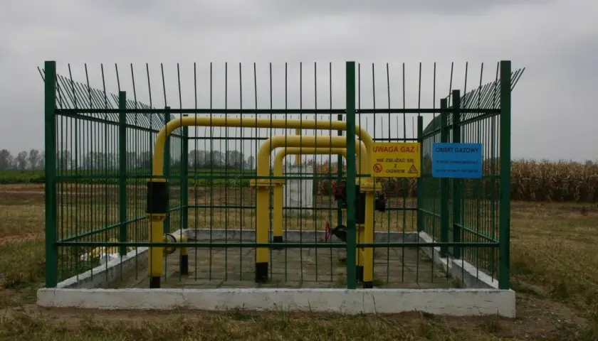 Ogrodzony obiekt gazowy z żółtymi rurami. Widać znaki ostrzegawcze. Obraz pokazuje odległość budynku od gazociągu wysokiego ciśnienia.