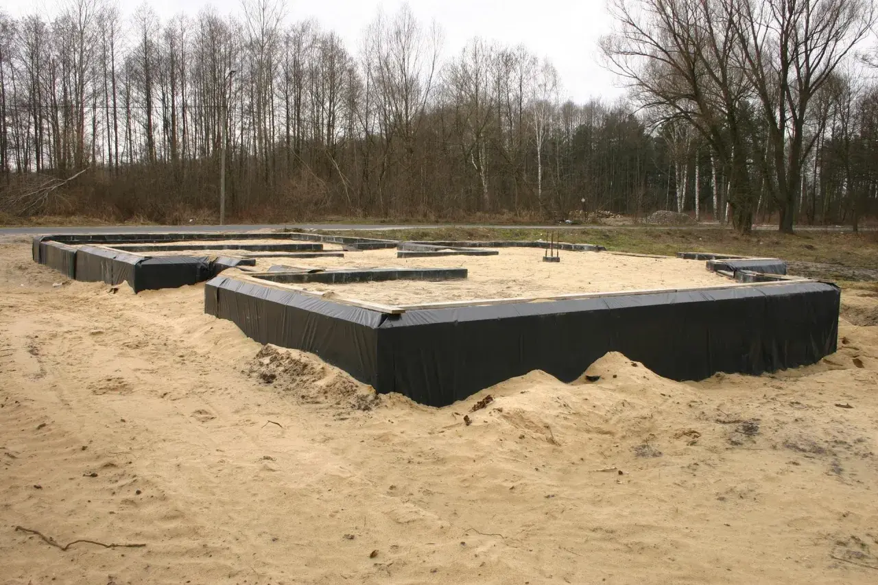 Fundament domu w piasku, przygotowany do wylania betonu. Czarna folia zabezpiecza przed wilgocią, a w przyszłości zapewni uszczelnienie przejścia rury przez fundament.