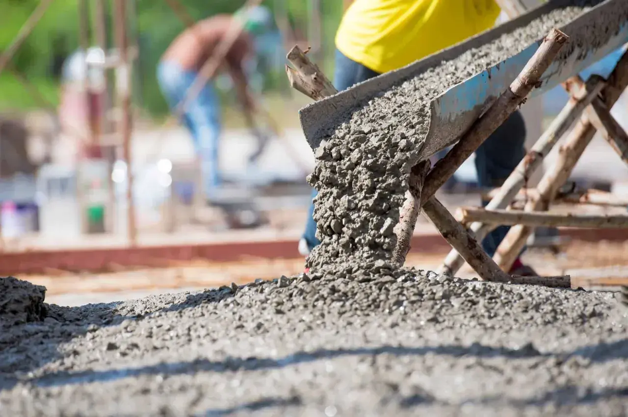 Beton wylewany z betoniarki na placu budowy. Obrazek ilustruje, jak obliczyć metry sześcienne betonu potrzebne do wylania fundamentów.