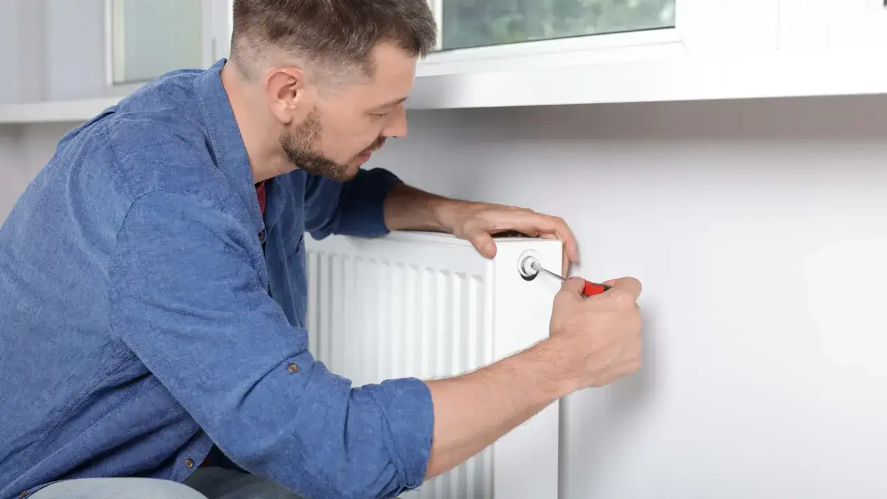 Mężczyzna odpowietrza grzejnik. Zastanawiasz się, od ktorego grzejnika zaczac odpowietrzanie? Zacznij od tego najniżej położonego w instalacji.