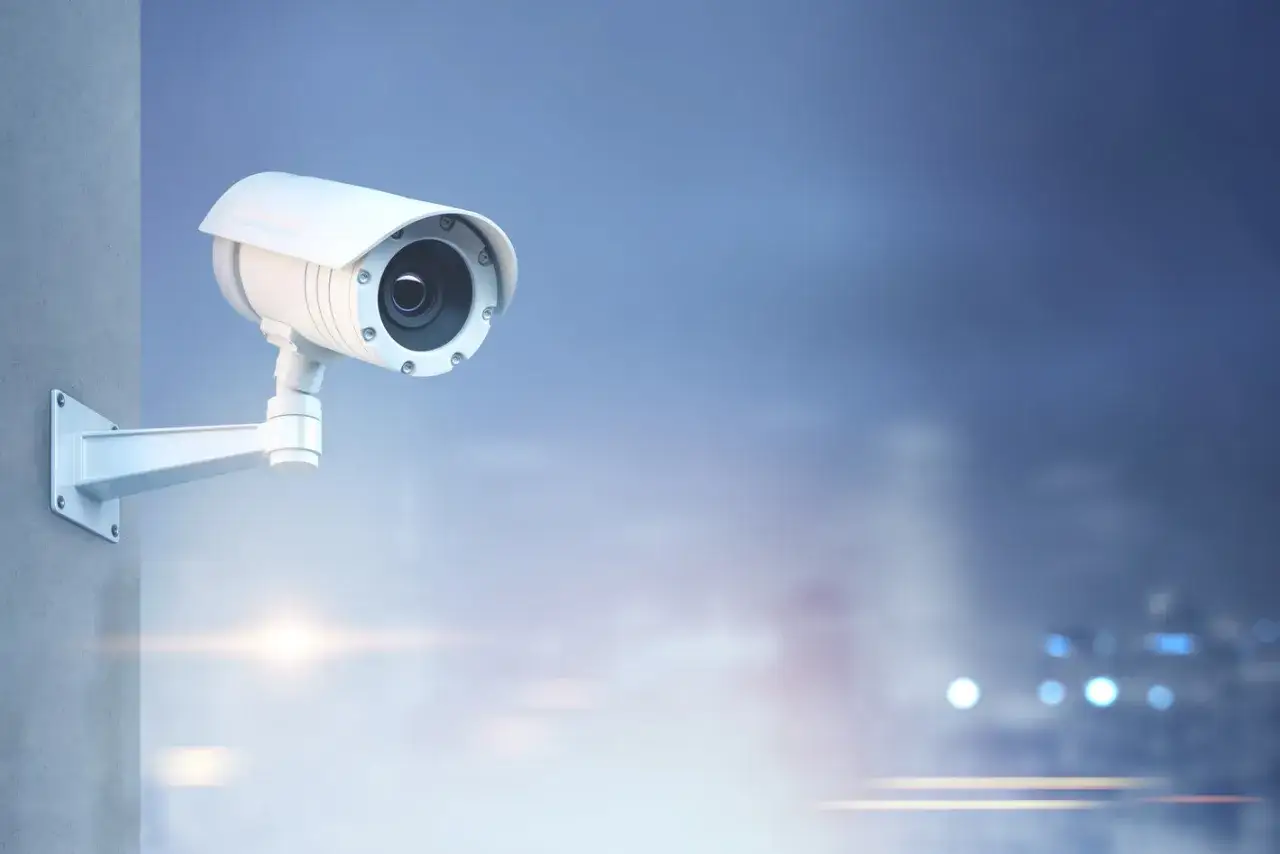 Biała kamera CCTV zamontowana na ścianie, monitorująca otoczenie. To właśnie cctv co to jest, czyli system nadzoru wizyjnego.
