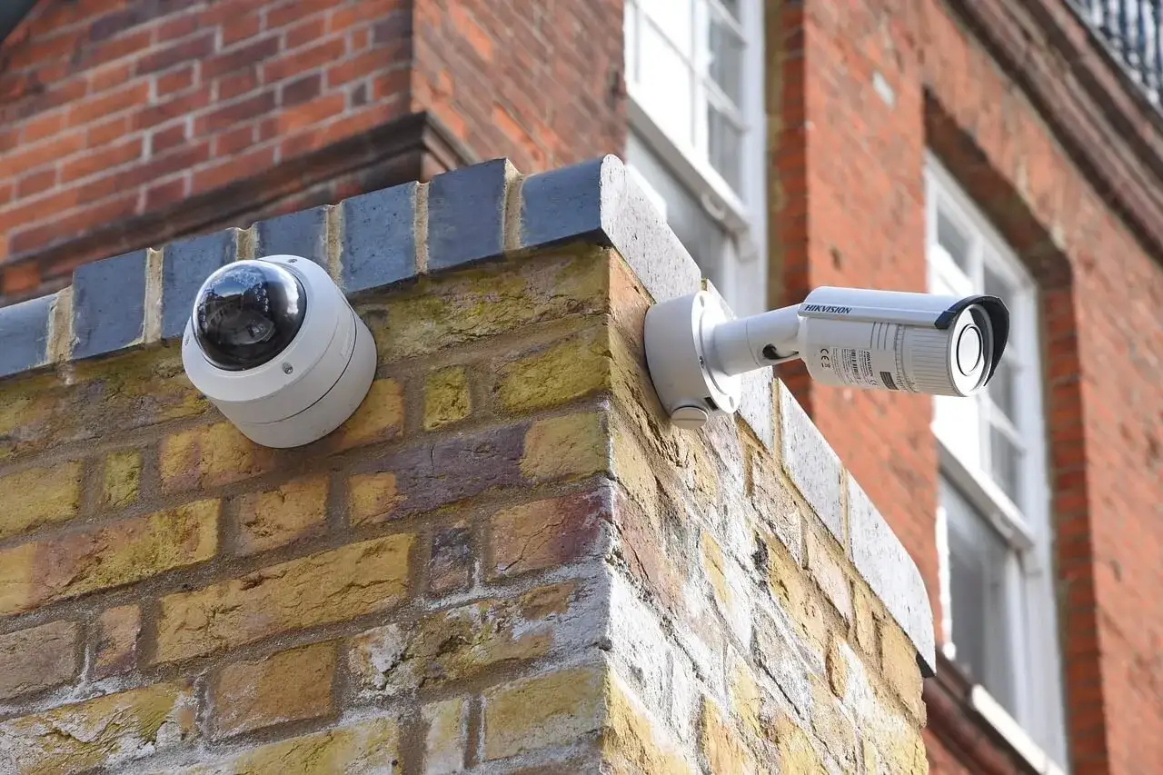 Dwie kamery CCTV zamontowane na rogu ceglanego budynku. Jedna to kopułkowa, druga to cylindryczna.